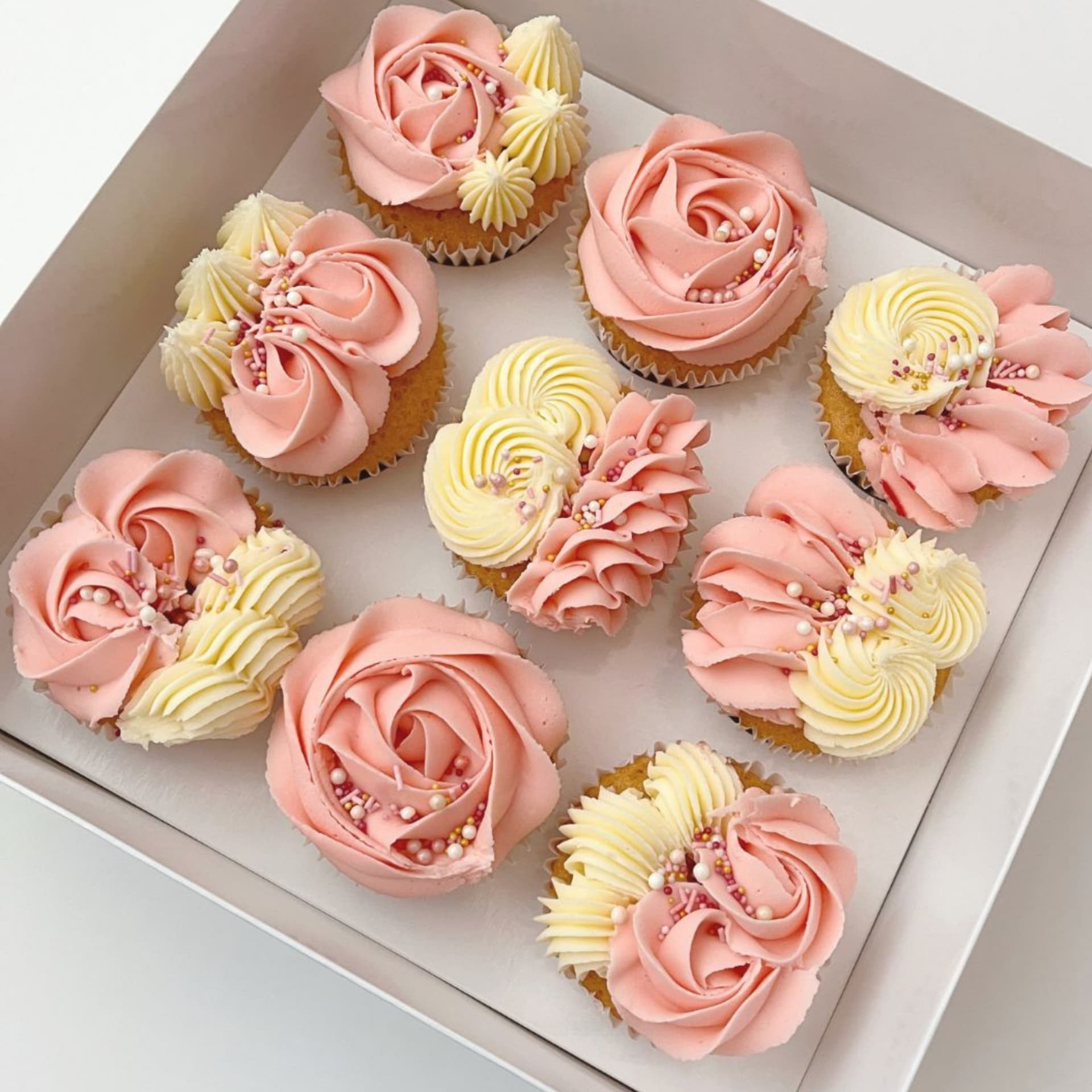 Box of pink and cream buttercream swirl cupcakes with sprinkles