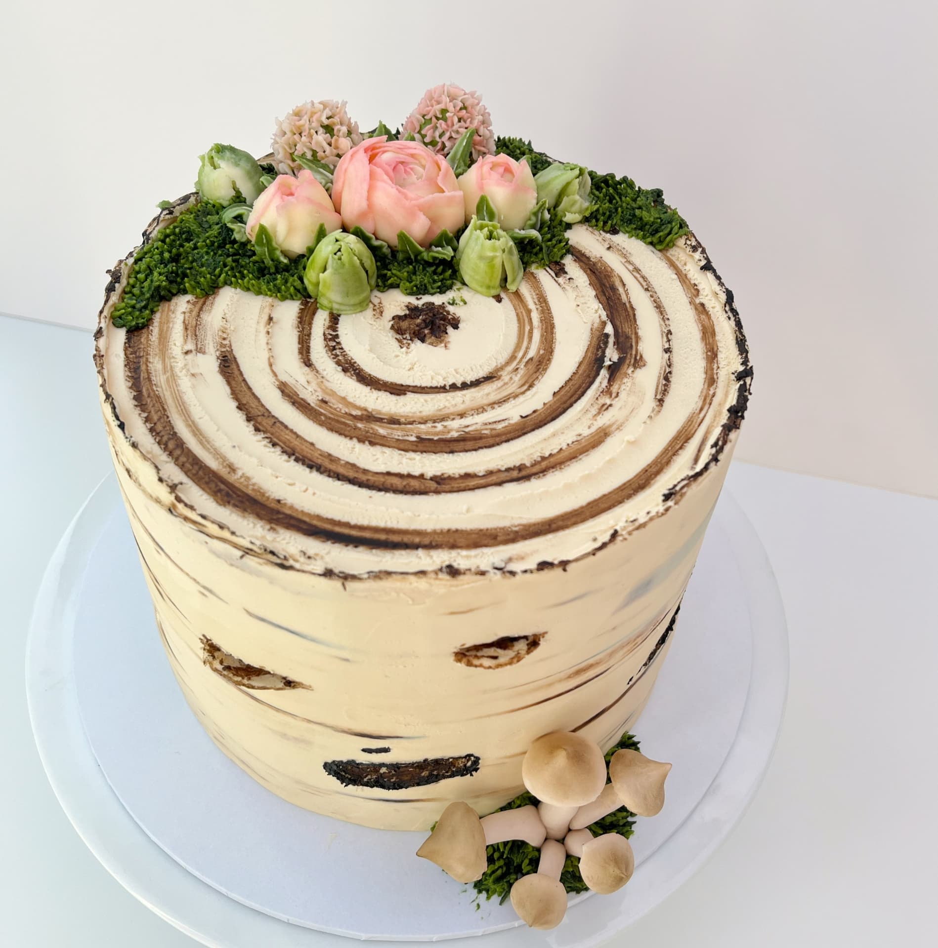 Award-winning birch tree stump celebration cake decorated with hand-modelled mushrooms, piped moss, and delicate buttercream flowers by Sharon Burchall.
