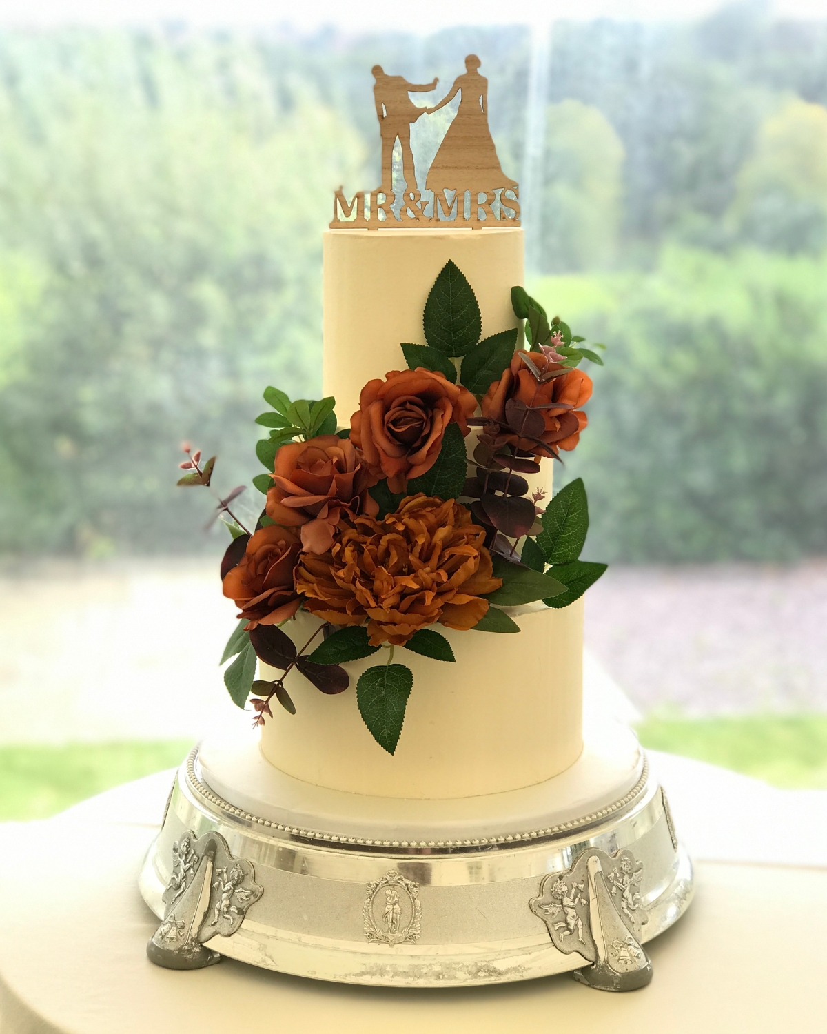 Three tier wedding cake with rust roses and a wooden Mr & Mrs topper