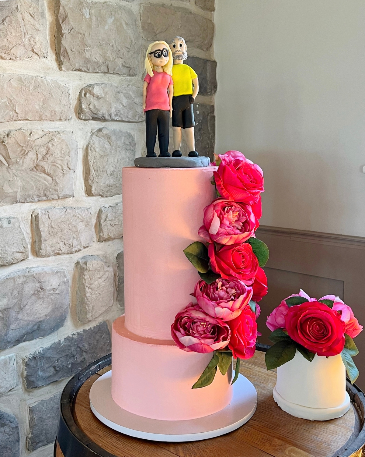 Pink two tier wedding cake with hand-modelled sugar figures and a matching cutting cake